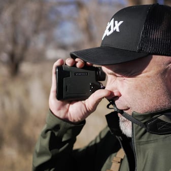 Bowhunter using handheld rangefinder in dense timber during stealthy spot-and-stalk bear hunt in Montana avalanche chute