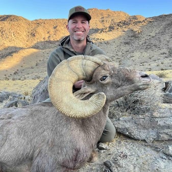 Hunter Brad Lucich posing with harvested desert bighorn sheep ram Eagle Eye in rocky California Cady Mountains after one-shot kill