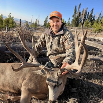 Hunter Darrin Hansen posing with large 5x6 mule deer buck featuring double split G2 in Wyoming open country after opening day rifle harvest